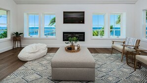 A living room with a large window overlooking the sea, a fireplace, a bean bag, and a wicker chair.