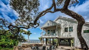 A two-story house with a covered patio, outdoor furniture, and a view of the ocean.