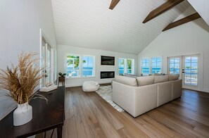 Un salón espacioso con un amplio ventanal con vistas al mar, un sofá color beige y un suelo de madera oscura.