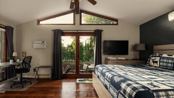 Un dormitorio con una cama grande, un escritorio con silla, un televisor y un balcón con vistas a árboles.