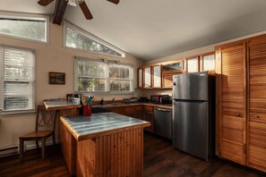 Une cuisine avec des meubles en bois, un réfrigérateur en acier inoxydable et une fenêtre équipée de stores.