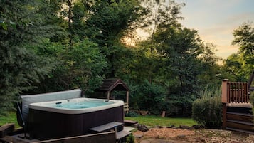 A hot tub in a wooded backyard with a wooden deck and a gazebo.