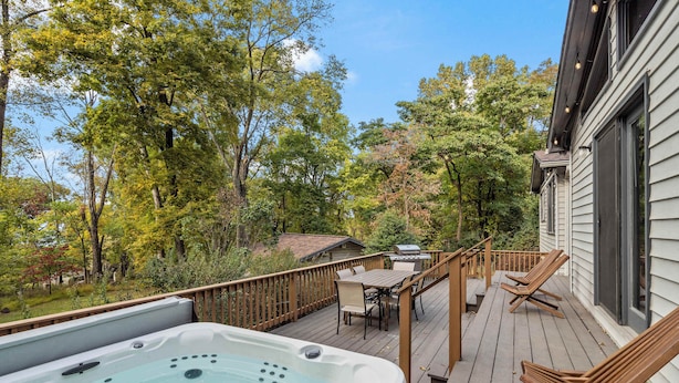 Una terraza de madera con un jacuzzi, mobiliario exterior y vistas a árboles.