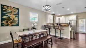 A modern kitchen with white cabinets, a stainless steel refrigerator, and a dining area with a wooden table and bench. - Centrally Located Spacious 3 BR Home (Tampa)