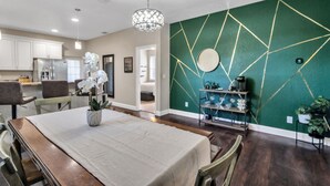 A dining area with a table set for four, a chandelier, and a green accent wall with geometric patterns. - Centrally Located Spacious 3 BR Home (Tampa)