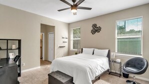 A bedroom with a bed, a desk, a chair, a ceiling fan, and a window with blinds. - Centrally Located Spacious 3 BR Home (Tampa)