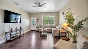 A living room with a flat-screen TV, a ceiling fan, a sofa, a coffee table, and a plant. - Centrally Located Spacious 3 BR Home (Tampa)