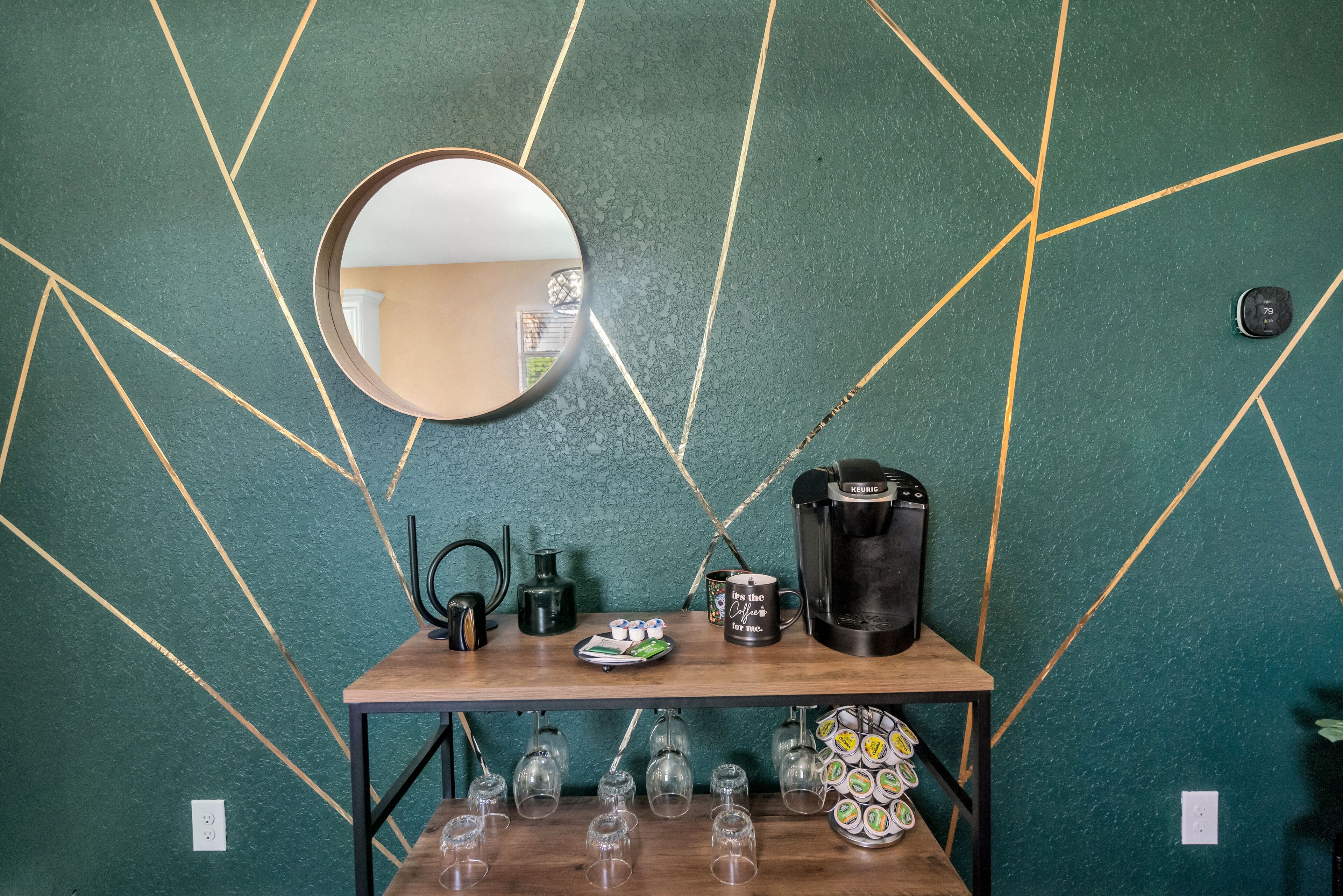 Una zona de bar con una cafetera, tazas, vasos y un plato de comida.
