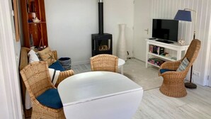 A cozy living room with a white table, wicker chairs, a bookshelf, a TV, and a fireplace.
