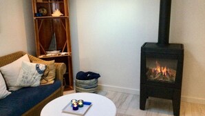 A living room with a sofa, a round coffee table, a bookshelf, and a wood-burning stove.