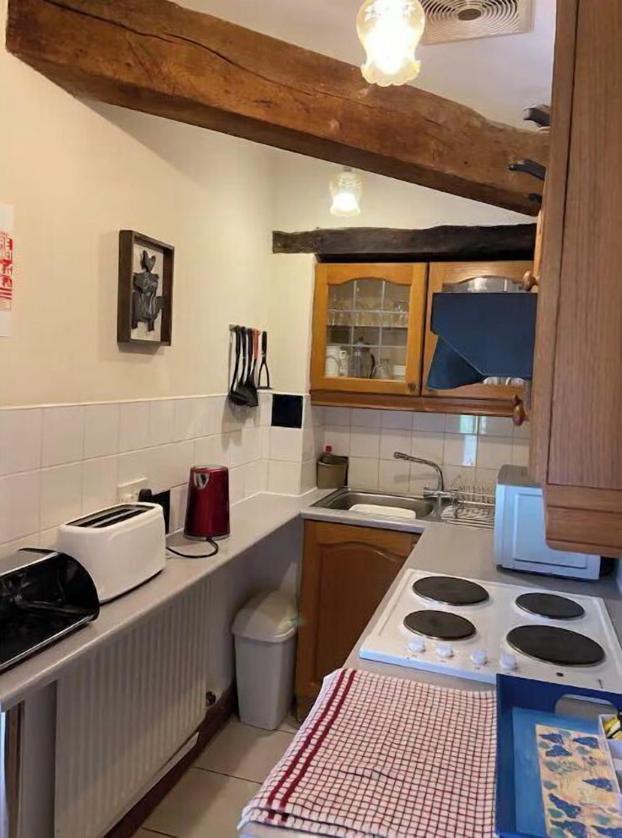 A compact kitchen with a wooden ceiling, a white tiled backsplash, a stove, a sink, and a toaster.