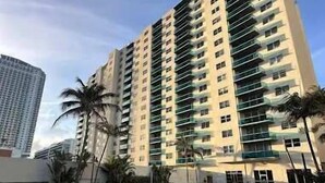 A high-rise hotel with a swimming pool, palm trees, and a clear sky.