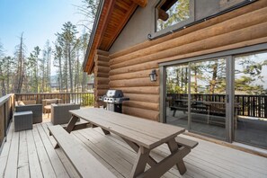 Eine Holzterrasse mit Picknicktisch, Sitzgelegenheiten und Grill.
