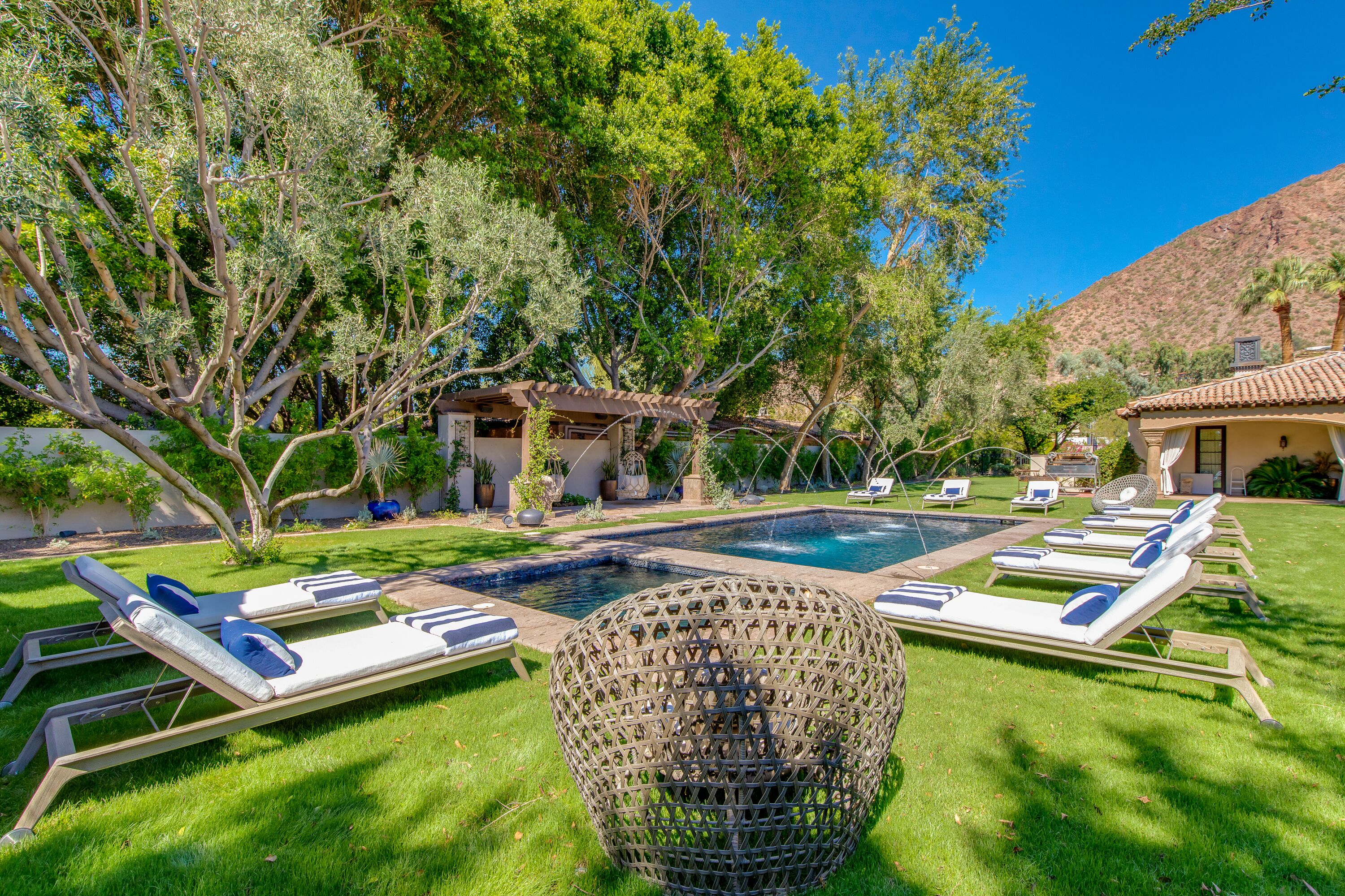 Zona de piscina con sillas de descanso y una esfera decorativa de mimbre.
