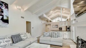 A spacious living area with a high ceiling and a kitchen in the background.