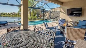 An outdoor patio with a pool, seating, and a TV. - Stunning Executive Home in Gated Community (Fort Myers)