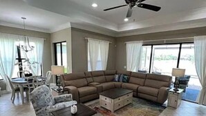 A spacious living room with a sectional sofa, a coffee table, and a dining area with a chandelier. - Stunning Executive Home in Gated Community (Fort Myers)