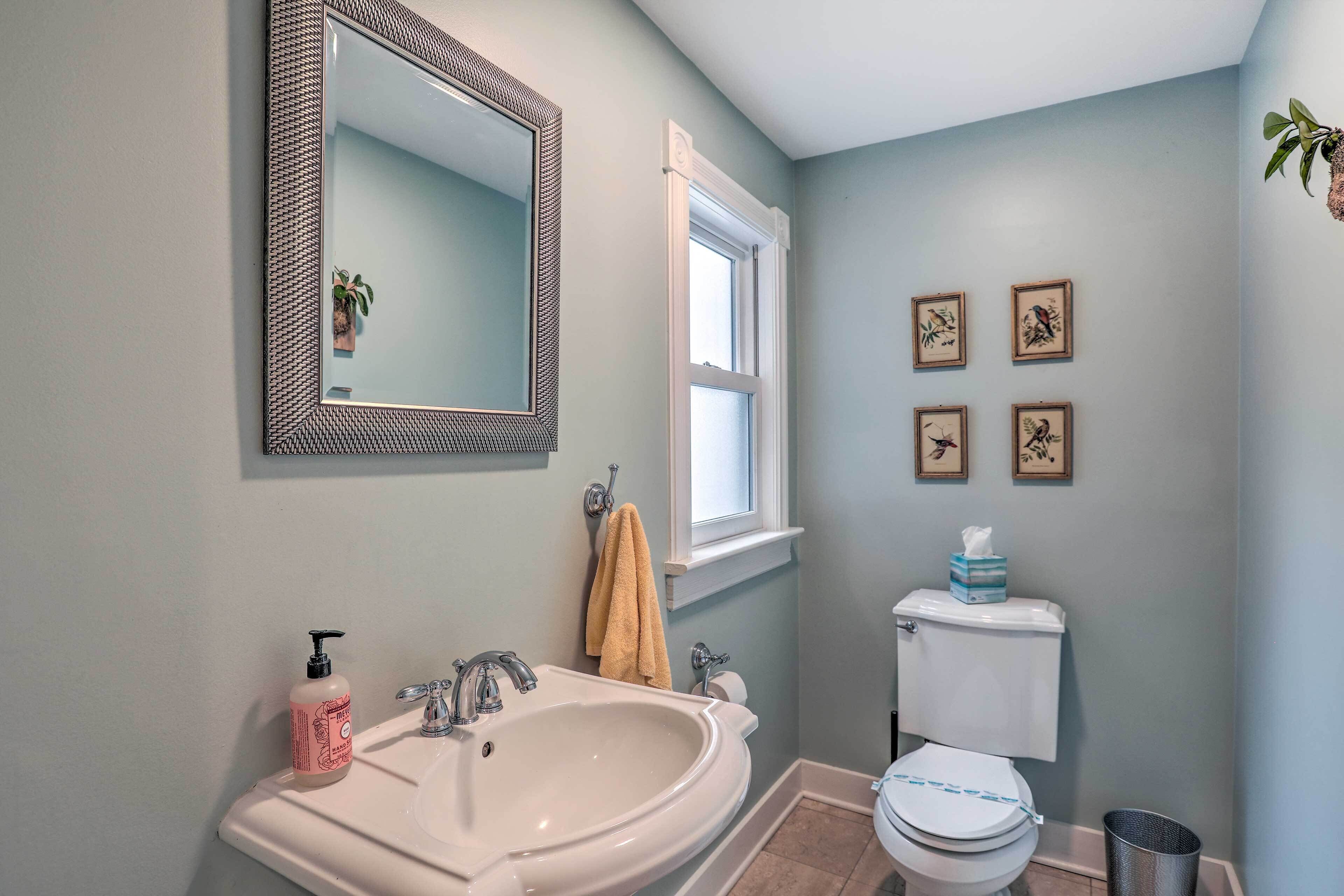 A bathroom with a sink, mirror, toilet, and framed pictures on the wall.