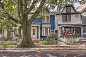 Una hilera de casas adosadas con un árbol grande al frente, un pequeño jardín y una calle.