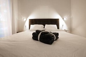 Una cama bien hecha con ropa de cama blanca y un juego de toallas negras en el centro.