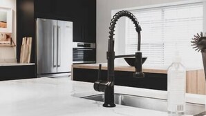 Eine moderne Küche mit einem schwarzen Wasserhahn, Edelstahlgeräten und einer weißen Arbeitsplatte.
