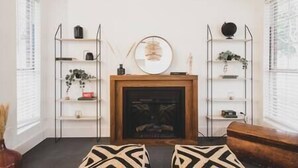 Ein Wohnzimmer mit Kamin, zwei nebeneinanderliegende Sofas und einem Couchtisch. An beiden Seiten des Kamins befinden sich Regale mit dekorativen Gegenständen.