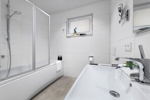 Uma casa de banho moderna com chuveiro separado por vidro, uma banheira branca grande e uma pia embutida.