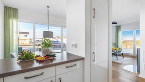 Una cocina moderna con armarios blancos, encimera de madera y vistas a la ciudad a través de amplios ventanales.