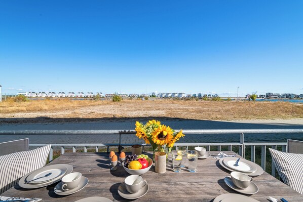 A dining table set with plates, bowls, and a vase of sunflowers, overlooking a body of water and a distant cityscape.