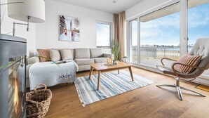 Una sala de estar moderna con un sofá, una mesa de centro y un sillón. Hay un ventanal con vistas a la ciudad.