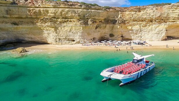 A boat with red seats docked at a beach with clear turquoise water and rocky cliffs in the background.