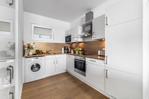 A modern kitchen with white cabinets, a built-in washing machine, a stove, and a microwave. - "Ocean Water" Baltic Sea vacation with a 3-minute walk to the beach, fireplace and sea view (Olpenitz)