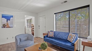 A living room with a blue sofa, patterned armchair, and a coffee table with a plant.