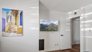 A room with a bed, a painting of a street scene, a mounted television, and a door leading to another room.