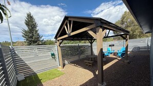 A covered outdoor seating area with a pergola structure, a picnic table, and blue chairs.