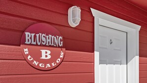 Un mur extérieur rouge avec une porte blanche et une enseigne sur laquelle on peut lire « BLUSHING B #BUNGALON ».