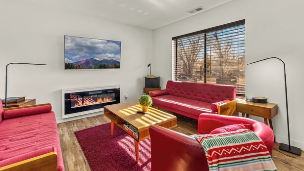 Un salon moderne avec un canapé rouge, une table basse en bois, une cheminée et une grande fenêtre équipée de stores.