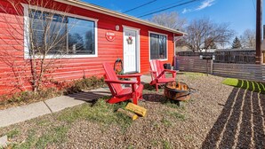 Un bâtiment rouge avec une porte et des fenêtres blanches, deux fauteuils Adirondack rouges, un foyer et une allée gravillonnée.