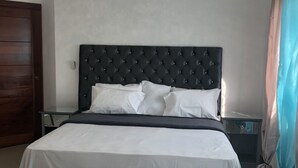 Ein ordentlich bezogenes Bett mit einem geblatteten Kopfteil, ein Nachttisch und ein Beistelltischchen mit einer Lampe.