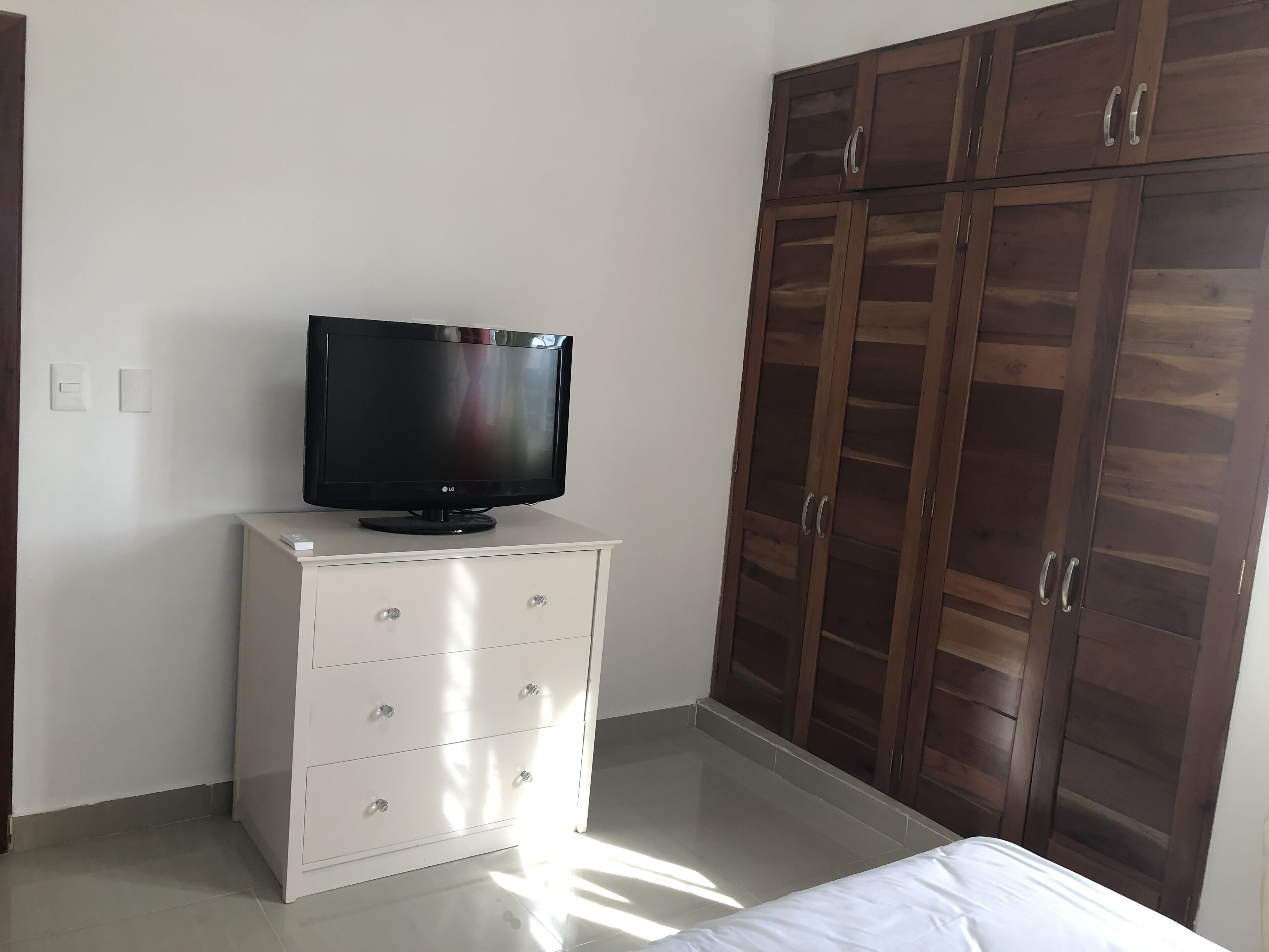 Ein Schlafzimmer mit einem Bett, einem Fernseher auf einer weißen Kommode und einem Holzschrank.