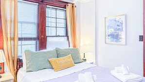 Cama bem arrumada com travesseiro que diz 'nosso lugar favorito', uma luminária de cabeceira e uma janela com persianas.