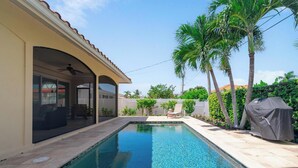 Ein Pool mit Grill, Palmen und einer überdachten Terrasse.