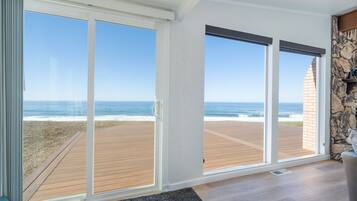 A room with large sliding glass doors leading to a wooden deck overlooking the ocean.