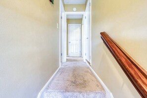 A carpeted hallway with a wooden handrail, leading to a white door at the end.