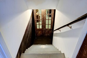 Una escalera de madera con barandilla metálica que lleva a una puerta con paneles de vidrio.