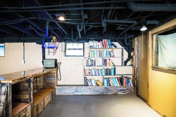 A room with a wooden bar, bookshelves, and exposed pipes on the ceiling.
