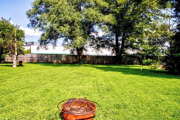 A backyard with a grassy lawn, a metal fire pit, and a wooden fence.