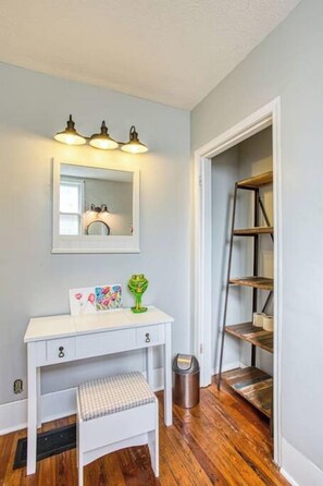 A white desk with a mirror above it, a small stool, and a trash can.