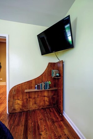 Una habitación con una pared de acento de madera, un televisor de pantalla plana montado y una estantería con libros y objetos decorativos.
