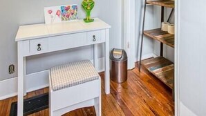 A white vanity with three wall-mounted lights, a mirror, a small bench, and a trash can.